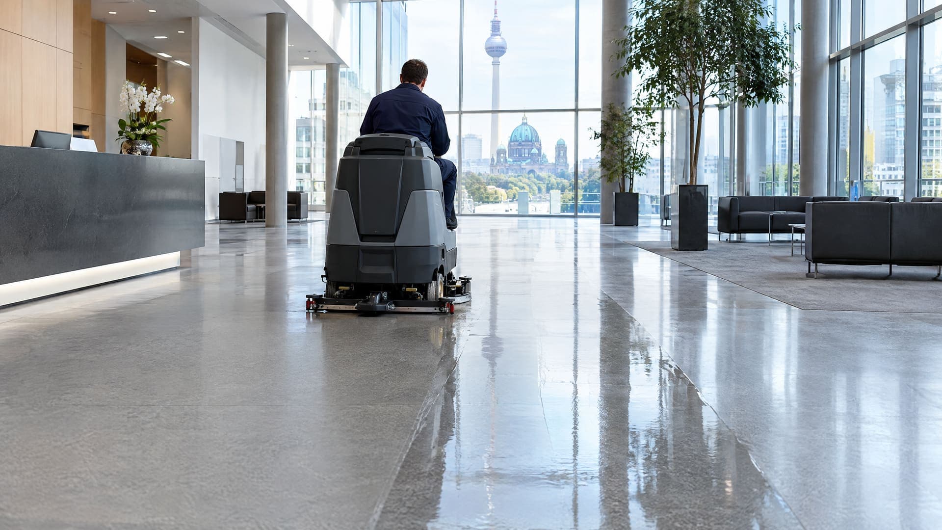 Aufsitz-Scheuersaugmaschine reinigt den hellen Steinboden einer Büro-Lobby